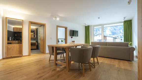 A modern living room with a large window and a view of the mountains. The room is brightly furnished with a dining table, chairs, and a couch. - Zwieselstein-Apart De Luxe - Zwieselstein
