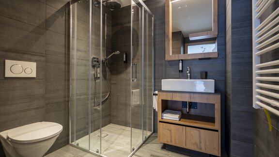 A modern bathroom with a glass shower and an elegant sink. The walls are in a dark tone, complemented by wooden details. - Zwieselstein-Apart De Luxe - Zwieselstein