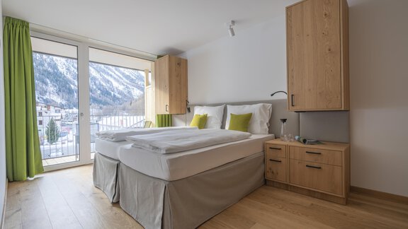 A modern bedroom with a cozy double bed and wooden furniture. Large windows offer a view of the mountains and plenty of daylight. - Zwieselstein-Apart De Luxe - Zwieselstein
