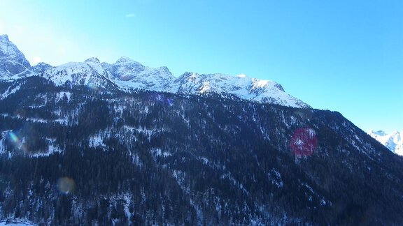 A wintry mountain landscape with snow-covered peaks and a clear blue sky. In the foreground, small buildings can be seen in a valley. - Berghof Schöpf - Gries