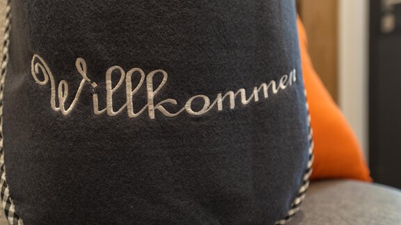 Ein dekorativer Kissenbezug in Grau mit der Aufschrift "Willkommen". Der Bezug hat einen eleganten und einladenden Look. - Apart Fiegl Längenfeld - Längenfeld