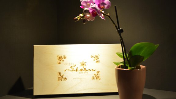 Eine schöne Orchidee in einem Topf steht neben einem eleganten Schild mit dem Namen "Siam". Der Hintergrund ist dunkel, was die Blumen und das Schild hervorhebt. - Hotel Stern - Längenfeld
