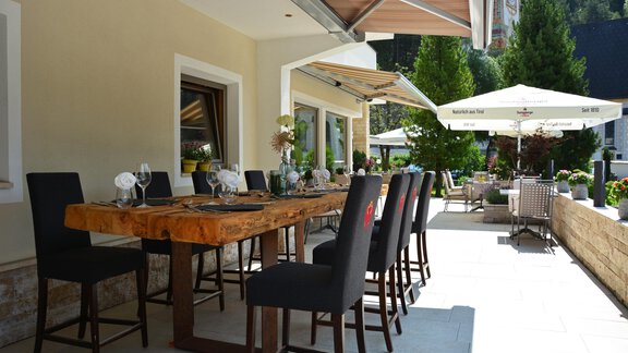 Ein stilvoller Außenbereich mit einem großen Holztisch und eleganten Stühlen. Sonnenschirme und Grünpflanzen schaffen eine einladende Atmosphäre. - Hotel Stern - Längenfeld