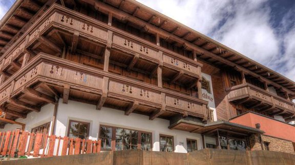 A beautiful chalet with a wooden balcony and a high roof. In the foreground lies snow and the sky is partly cloudy. - Hotel-Garni Pirchhütt - Obergurgl 