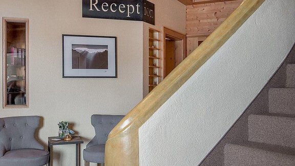 An inviting reception area with modern chairs and a beautiful staircase. A picture is hanging on the wall along with a sign that says "Reception". - Hotel-Garni Pirchhütt - Obergurgl 