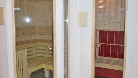 Two sauna cabins in a wellness area. The left cabin has a wooden bench and glass door, while the right cabin is designed in red. - Pension Angern - Obergurgl 