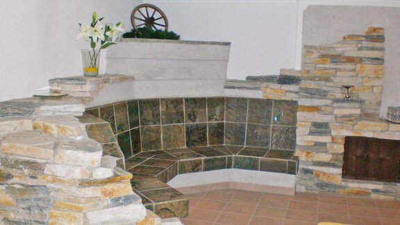 A modern wellness area with a seating arrangement made of natural stone. The walls are clad in gray and brown stones, and there is a bouquet of flowers in a vase. - Pension Angern - Obergurgl 