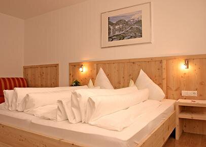 A cozy bedroom with a large bed and wooden details. A picture of a landscape hangs on the wall. - Pension Angern - Obergurgl 