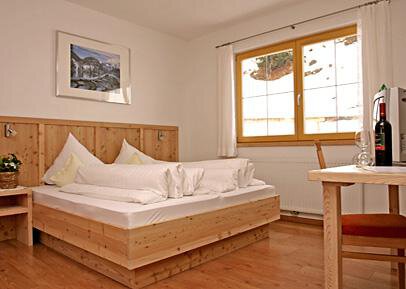A cozy bedroom with a wooden double bed and a bright, inviting atmosphere. A table with drinks and a window offer a view outside. - Pension Angern - Obergurgl 