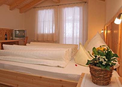 A cozy room with a large bed and wooden decor. On the nightstand, there is a flower pot with fresh flowers. - Pension Angern - Obergurgl 