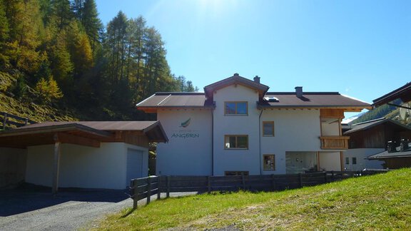 A modern house in a green environment, surrounded by trees. The sun shines brightly in the clear sky. - Pension Angern - Obergurgl 