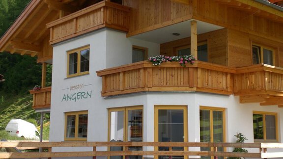 A modern wooden house with several balconies and colorful flowers. The facade is bright and friendly, surrounded by green nature. - Pension Angern - Obergurgl 