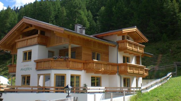 A modern chalet in Alpine style with wooden balconies and bright walls. Surrounded by green mountains and blue sky. - Pension Angern - Obergurgl 