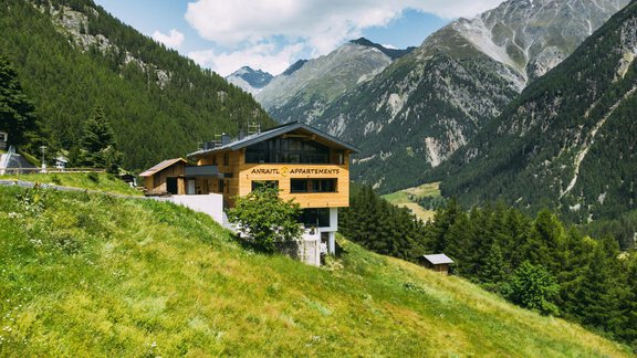 A modern chalet on a green meadow in the mountains. The surroundings are framed by majestic mountains and a blue sky. - Anraitl Appartements Sölden - Sölden