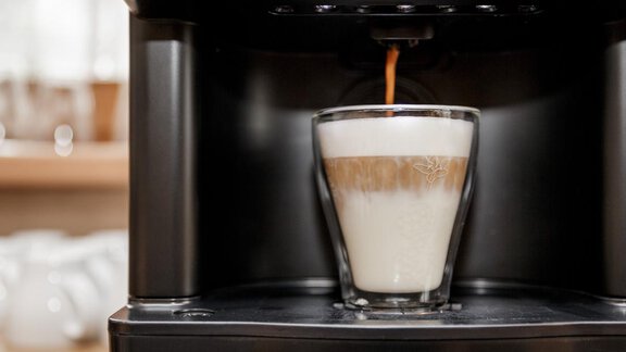 A modern coffee machine prepares a coffee in a glass. One can see a beautiful layering of coffee and milk. - Apart Garni Enzian - Sölden | © RudiWyhlidal