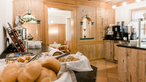 A cozy kitchen with wood paneling and a selection of rolls. In the background, coffee machines and inviting seating options can be seen. - Apart Hotel Garni Alt Kaisers - Sölden