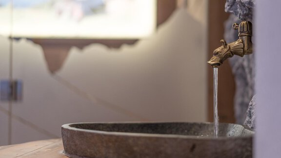 An elegant stone sink with a golden faucet. Water flows gently from the faucet into the basin. - Apart Hotel Garni Alt Kaisers - Sölden