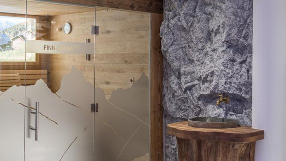 A modern sauna with a glass door and wood decor. Next to the sauna is a stylish wash area made of wood and stone. - Apart Hotel Garni Alt Kaisers - Sölden