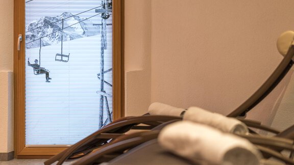 A relaxation room with lounge chairs and towels. Through the window, a ski lift can be seen against a backdrop of snow-covered mountains. - Apart Hotel Garni Alt Kaisers - Sölden
