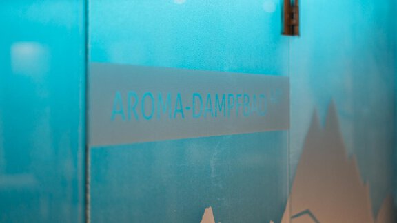 A blue room with a glass panel that says "AROMA STEAM ROOM." In the background, stylized mountain forms are visible. - Apart Hotel Garni Alt Kaisers - Sölden