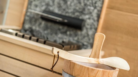 A wooden vessel with a spoon is standing on a stone countertop. Kitchen appliances are visible in the background. - Apart Hotel Garni Alt Kaisers - Sölden