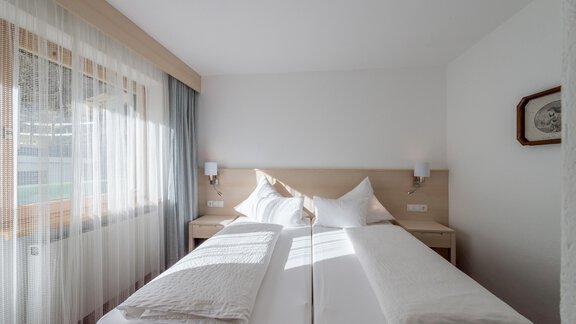 A cozy bedroom with two single beds and plenty of natural light. The walls are bright and the furnishings are modern and simple. - Apart Hotel Garni Wieser - Sölden