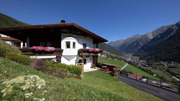 A picturesque house in the mountains with colorful flowers on the balcony. The surroundings feature a green meadow and majestic mountains in the background. - Appartement Harmonie - Sölden