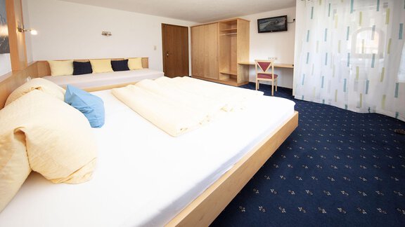 A modern hotel room with a large bed, a sofa, and a desk. The walls are light, and the room has blue carpeting. - Appartement Harmonie - Sölden