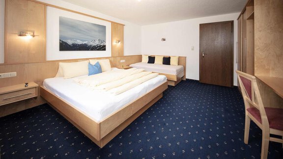 A bright hotel room with two beds and a cozy atmosphere. A picture of mountains hangs on the wall, and the floor is covered with a blue carpet. - Appartement Harmonie - Sölden