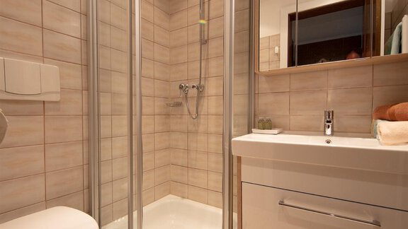 A modern bathroom with a shower and a sink. The walls are light tiled and a towel is lying on the floor. - Appartement Harmonie - Sölden