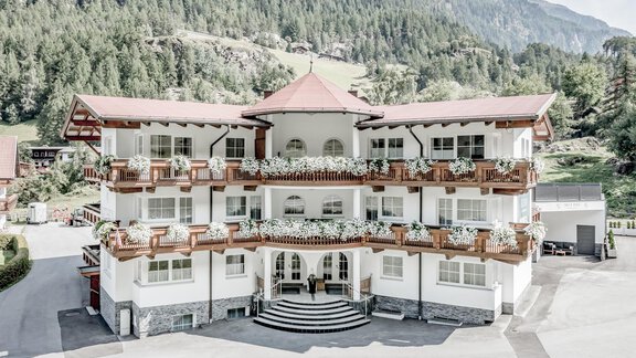 A charming hotel building with a distinctive roof and balconies. Surrounded by green mountains and trees, it offers an idyllic view. - Appartementhaus Kathrin - Sölden