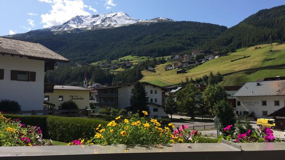 A picturesque mountain landscape with snow-covered peaks and green meadows. Colorful flowers adorn the foreground and traditional buildings are visible. - Appt. Ideal - Sölden