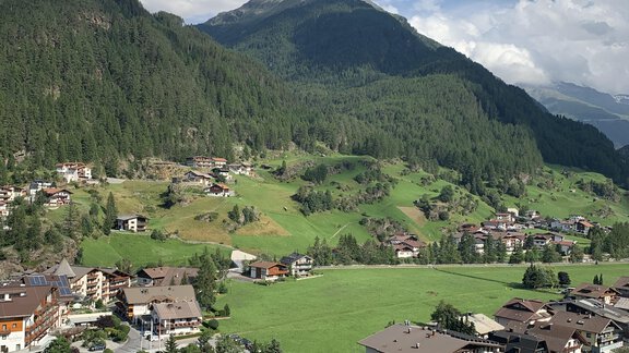 A picturesque mountain landscape with green meadows and surrounding mountains. In the foreground, there is a small village with traditional houses. - Appt. Ideal - Sölden