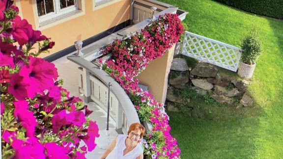 A person is standing on a balcony, surrounded by colorful plants and flowers. The well-maintained garden and the decorative facade give the scene an inviting atmosphere. - Appt. Ideal - Sölden