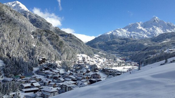 A snowy landscape with a small village and high mountains in the background. The sky is clear and blue. - Brandlehof - Sölden