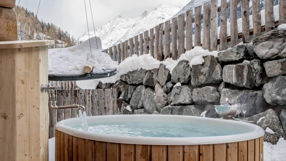A cozy wooden hot tub surrounded by snow-covered mountains. The rustic charm and tranquil surroundings invite relaxation. - Chalet Resort Sölden - Sölden