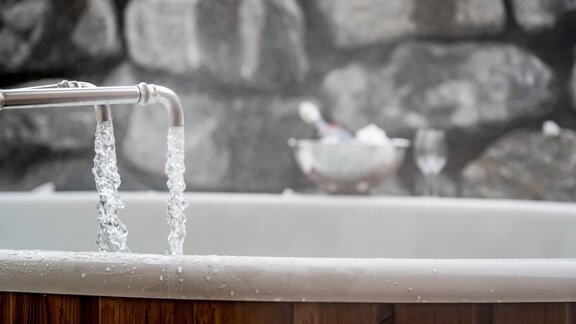 A wooden bath with bubbling water and a stone background. Glasses and a bowl are visible in the background. - Chalet Resort Sölden - Sölden