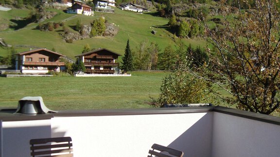 A terrace with a wooden table and chairs, surrounded by a beautiful mountain panorama. In the background, traditional chalets and green meadows can be seen. - Ferienappartements Linserhof - Sölden
