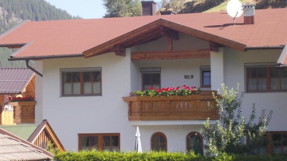 A cozy house with a balcony decorated with flowers. In the background, green hills and mountains can be seen. - Gstrein Andreas - Sölden