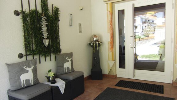 A bright entrance area with modern furniture and decorative elements. Two cushions with deer motifs are placed on the seating. - Haus Amaris - Sölden