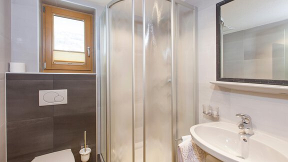 A modern bathroom with a shower, a sink, and a toilet. There is a window that provides natural light. - Haus Bergblick - Sölden