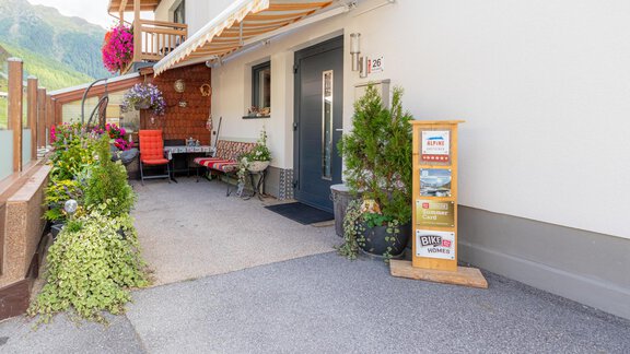 A cozy entrance area with plants and a small table. Next to the front door is an information stand. - Haus Edmund - Sölden