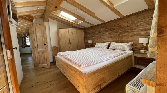 A cozy bedroom with a large wooden bed and beautiful wood decor. The ceiling has visible wooden beams and there is plenty of daylight coming in through the windows. - HAUS ERIKA apartments - Sölden