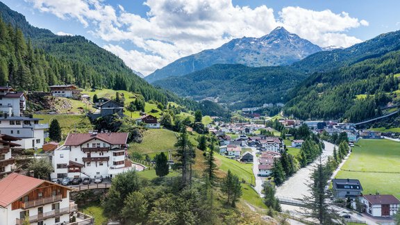 A picturesque mountain village surrounded by green hills and majestic mountains. The clouds are partially visible, and the landscape exudes a calm atmosphere. - Haus Fontana - Sölden