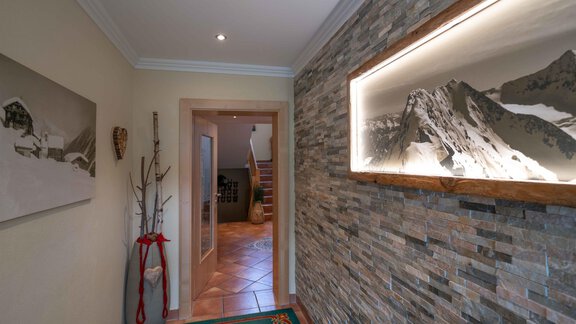 An inviting hallway with a stone-element wall and a illuminated landscape picture. The floor is tiled and a colorful rug adds to the coziness. - Haus Fridolin - Sölden