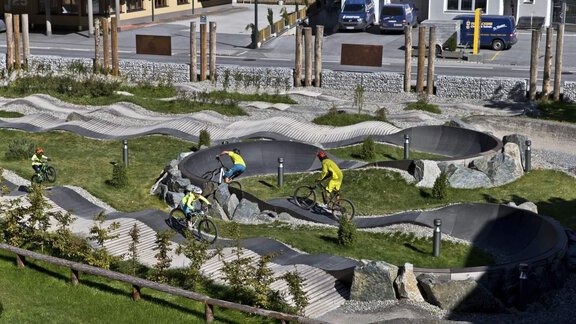 A stylish mountain bike trail with curves and hills. Several cyclists are riding through the green landscape. - Haus Gabriela - Sölden