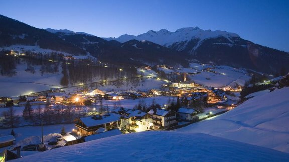 A snowy mountain landscape with a small village in the evening light. The lights of the village twinkle between the snow-covered houses. - Haus Gabriela - Sölden