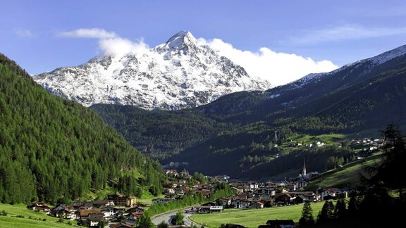 A picturesque mountain landscape with snow-covered peaks and a green valley. The small village in the middle is surrounded by trees. - Haus Gabriela - Sölden