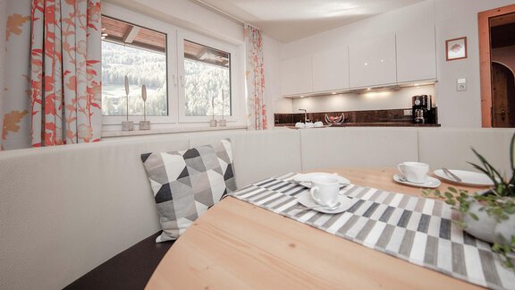 A bright kitchen with a round table and cushions. The windows offer a view of a green landscape. - Haus Ingrid - Sölden
