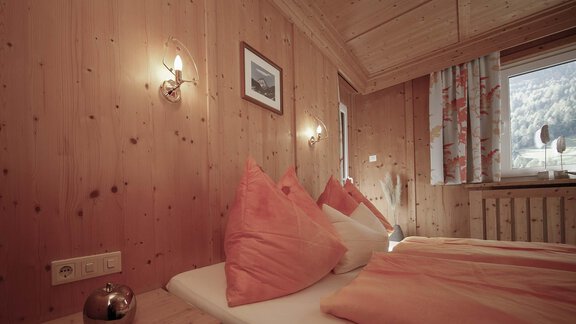 A cozy bedroom with wooden paneling and large cushions. The window offers a view of nature and the window decoration is bright and cheerful. - Haus Ingrid - Sölden